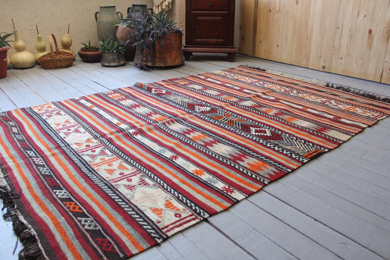 May include: A colorful striped rug with geometric patterns in shades of red, orange, white, and black. The rug has a fringe border and is laid out on a wooden floor.