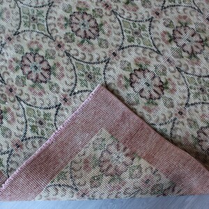 May include: A vintage rug with a floral pattern in shades of pink, green, and beige. The rug has a pink border and is woven with a fine texture.
