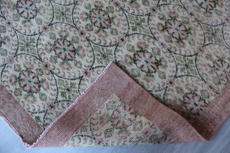 May include: A vintage rug with a floral pattern in shades of pink, green, and beige. The rug has a pink border and is woven with a fine texture.