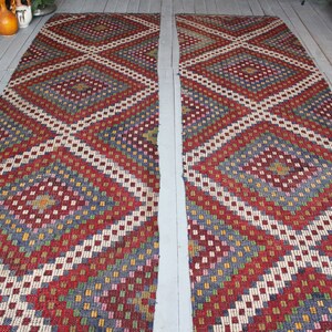 Op de afbeelding: Twee lange, smalle, rood, wit, blauw en groene gepatroneerde tapijten met een ruitpatroon. De tapijten liggen op een houten vloer.