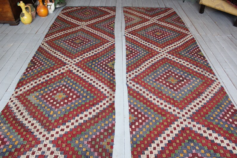 Op de afbeelding: Twee lange, smalle, rood, wit, blauw en groene gepatroneerde tapijten met een ruitpatroon. De tapijten liggen op een houten vloer.