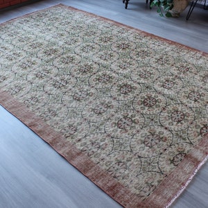 May include: A vintage rug with a cream background and a repeating pattern of green and pink floral motifs. The rug has a distressed, worn look and a reddish-brown border.
