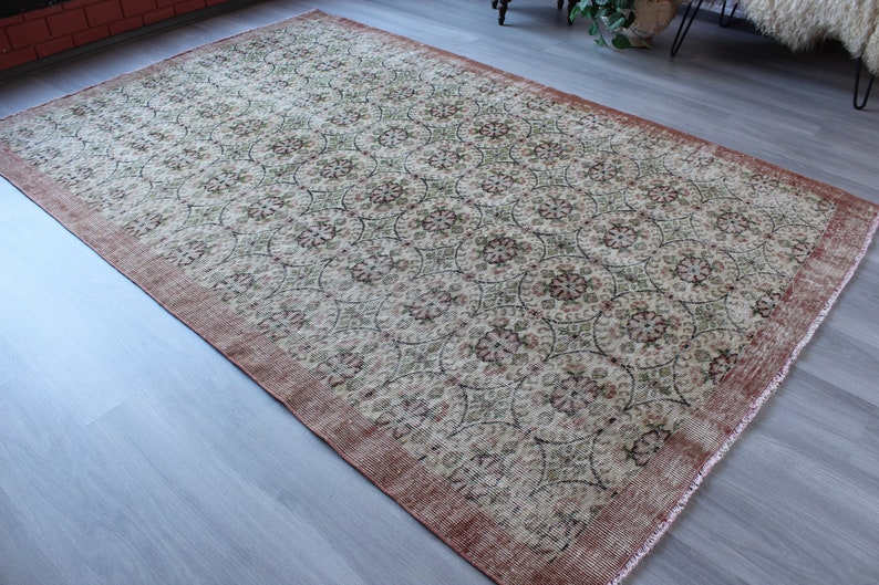 May include: A vintage rug with a cream background and a repeating pattern of green and pink floral motifs. The rug has a distressed, worn look and a reddish-brown border.