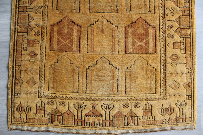 May include: A vintage prayer rug with a traditional design featuring arches and geometric patterns in shades of brown and beige.
