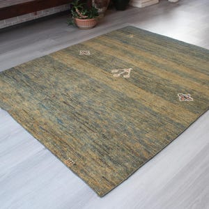 Op de afbeelding: Een groen en bruin vloerkleed met een subtiel patroon. Het kleed heeft een verweerde look en is gemaakt van een zacht, pluche materiaal.