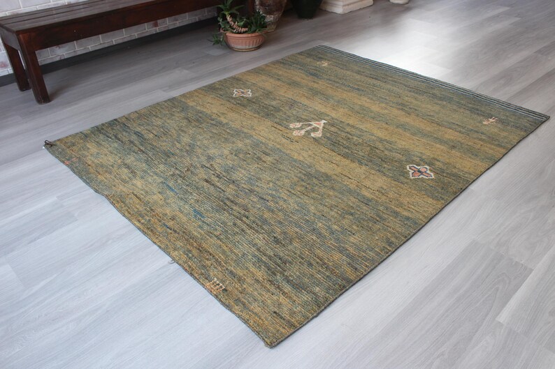 Op de afbeelding: Een groen en bruin vloerkleed met een subtiel patroon. Het kleed heeft een verweerde look en is gemaakt van een zacht, pluche materiaal.