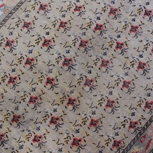 May include: A beige rug with a floral pattern in shades of pink, black, and white. The rug has a border with a geometric design.