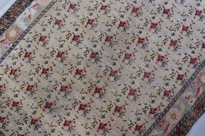 May include: A beige rug with a floral pattern in shades of pink, black, and white. The rug has a border with a geometric design.