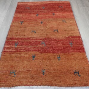 May include: A hand-woven rug with a red and orange color scheme. The rug has a geometric pattern with small blue accents.
