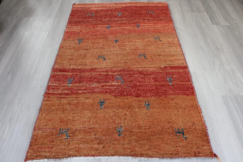 May include: A hand-woven rug with a red and orange color scheme. The rug has a geometric pattern with small blue accents.