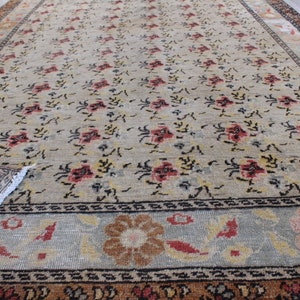 May include: A vintage rug with a floral pattern in shades of beige, brown, red, and black. The rug has a border with a geometric design.
