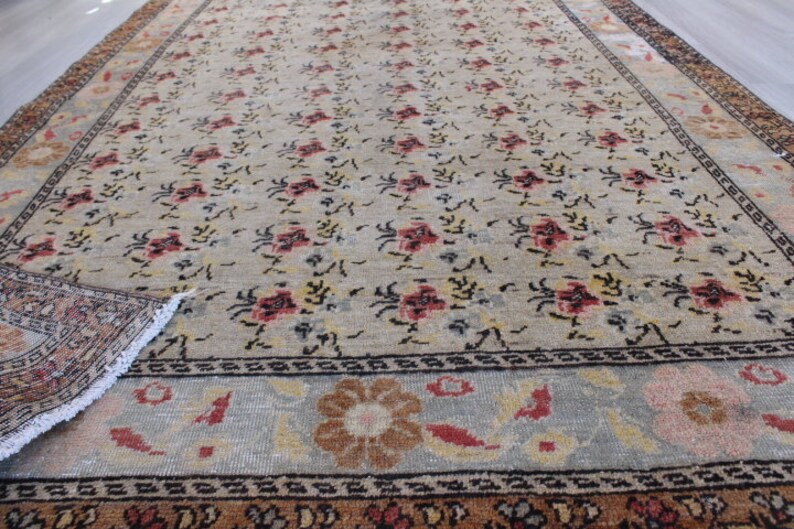 May include: A vintage rug with a floral pattern in shades of beige, brown, red, and black. The rug has a border with a geometric design.