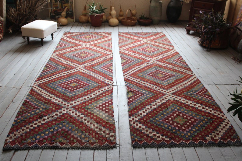 Op de afbeelding: Twee rode, witte en blauwe tapijten met een geometrisch ontwerp. De tapijten liggen op een witte houten vloer.