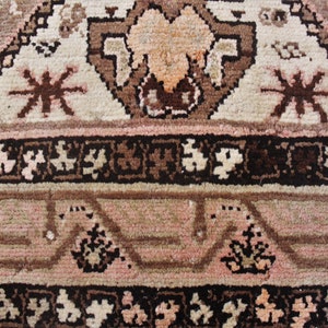 May include: Close-up of a brown and pink patterned rug with intricate details. The rug has a geometric design with floral motifs and a central medallion. The rug is made of wool and has a soft texture.