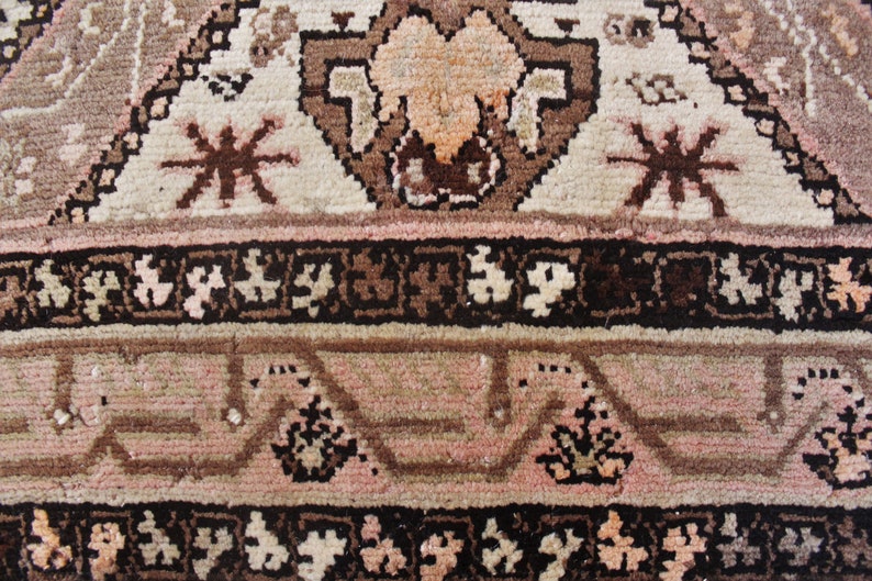 May include: Close-up of a brown and pink patterned rug with intricate details. The rug has a geometric design with floral motifs and a central medallion. The rug is made of wool and has a soft texture.