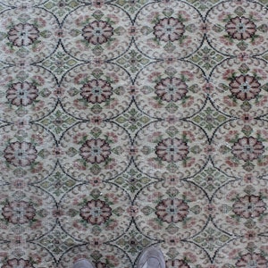 May include: A vintage rug with a cream background and a repeating pattern of pink and green floral motifs.