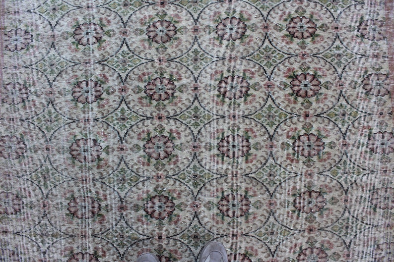 May include: A vintage rug with a cream background and a repeating pattern of pink and green floral motifs.