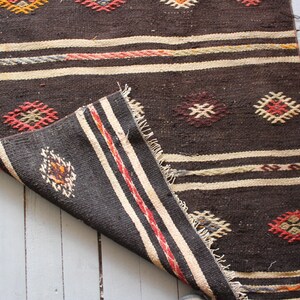 May include: A brown and white woven rug with geometric patterns in red, orange, and yellow. The rug is folded in half, showing the underside of the fabric.