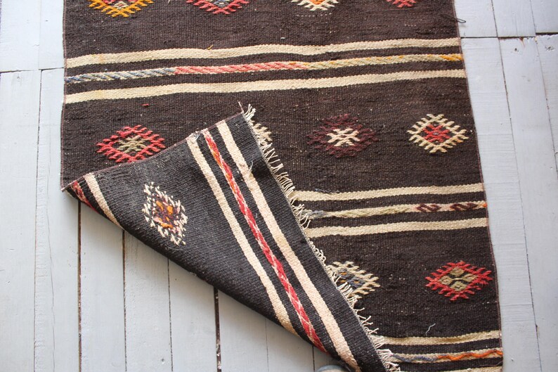 May include: A brown and white woven rug with geometric patterns in red, orange, and yellow. The rug is folded in half, showing the underside of the fabric.