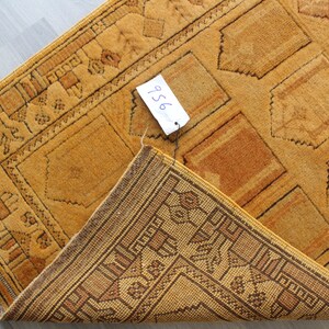May include: A close-up of a folded, yellow and brown patterned rug with a price tag that says "956".