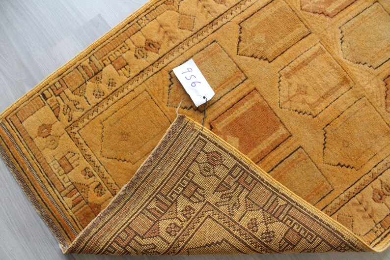 May include: A close-up of a folded, yellow and brown patterned rug with a price tag that says "956".