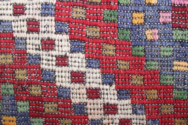 Op de afbeelding: Close-up van een kleurrijk geweven stof met een geometrisch patroon. De stof is gemaakt van draden in verschillende kleuren, waaronder rood, blauw, groen en geel.
