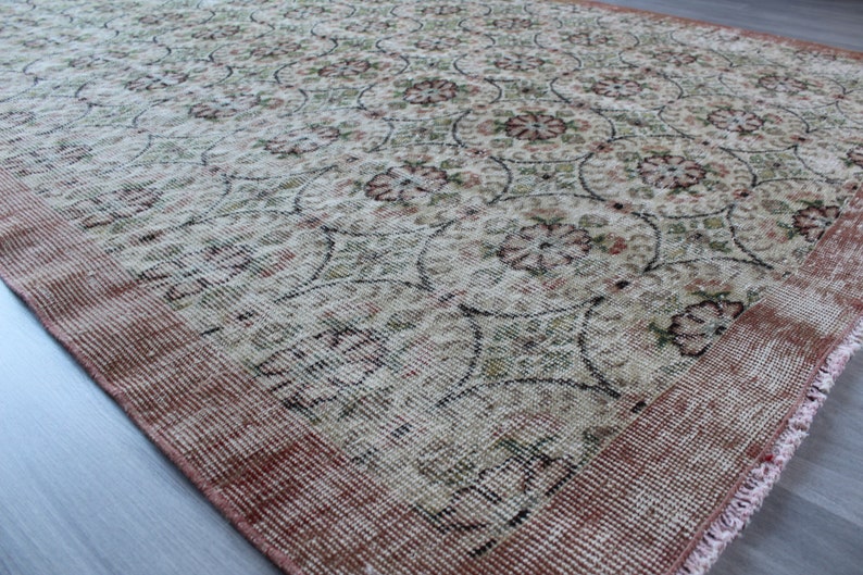 May include: A vintage rug with a floral pattern in shades of pink, green, and white. The rug has a fringed edge and a worn, distressed look.
