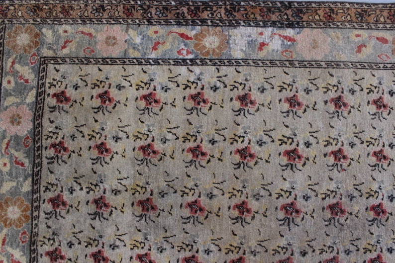 May include: A vintage rug with a beige background and a repeating pattern of small, stylized flowers in shades of red, black, and yellow. The rug has a border with a floral design in shades of pink, blue, and white.