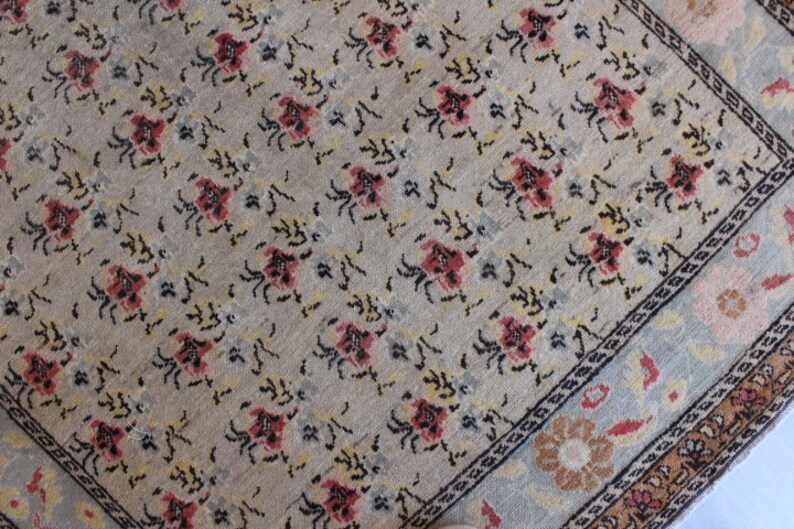 May include: A beige rug with a repeating pattern of small, stylized flowers in shades of red, pink, yellow, and black. The rug has a border with a floral design in shades of blue, pink, and brown.