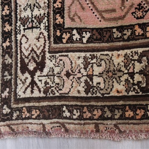 May include: Close-up of the bottom edge of a pink and brown patterned rug with a fringe. The rug has a floral design with intricate details.