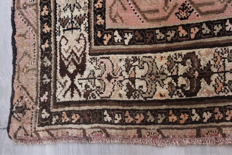 May include: Close-up of the bottom edge of a pink and brown patterned rug with a fringe. The rug has a floral design with intricate details.