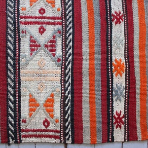 May include: A close-up of a colorful woven rug with intricate patterns in shades of red, orange, black, and white.