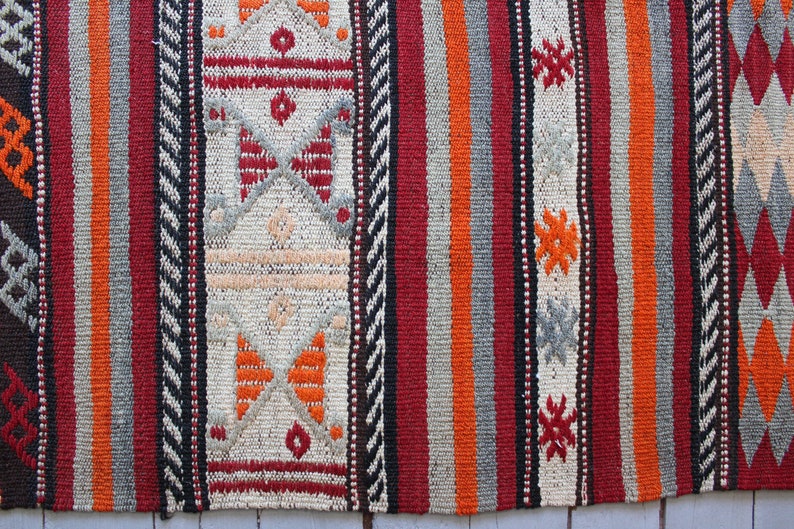 May include: A close-up of a colorful woven rug with intricate patterns in shades of red, orange, black, and white.