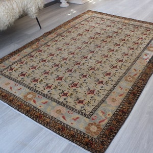 May include: A vintage rug with a cream background and a floral pattern in shades of red, brown, and blue. The rug has a border with a geometric design in brown and black.
