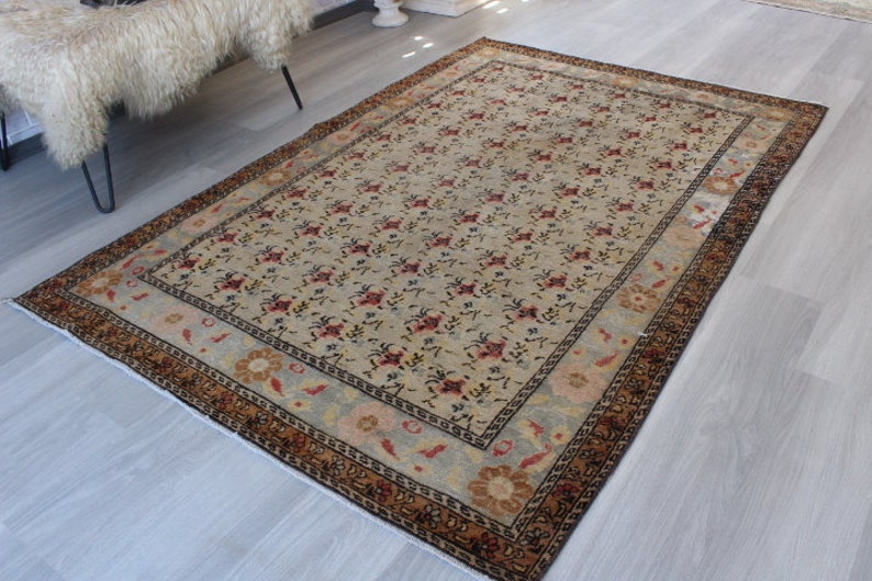 May include: A vintage rug with a cream background and a floral pattern in shades of red, brown, and blue. The rug has a border with a geometric design in brown and black.
