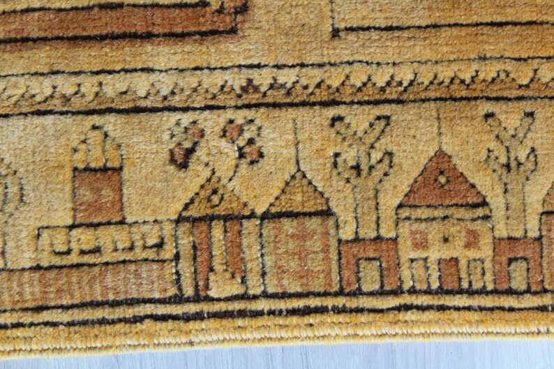 May include: Close-up of a beige rug with a brown border. The rug has a repeating pattern of stylized houses and trees.