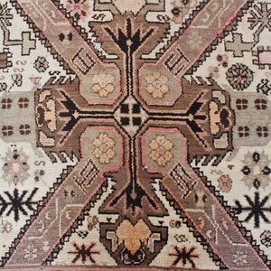May include: A vintage rug with a geometric pattern in shades of brown, pink, and white. The rug features a central medallion with a cross-shaped design and intricate details.
