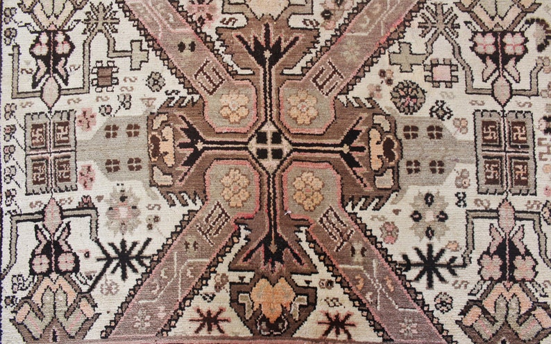 May include: A vintage rug with a geometric pattern in shades of brown, pink, and white. The rug features a central medallion with a cross-shaped design and intricate details.