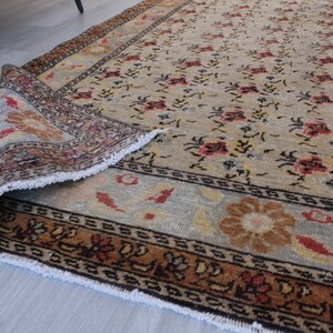 May include: A vintage rug with a floral pattern in shades of beige, brown, and red. The rug has a fringed edge and a detailed border.