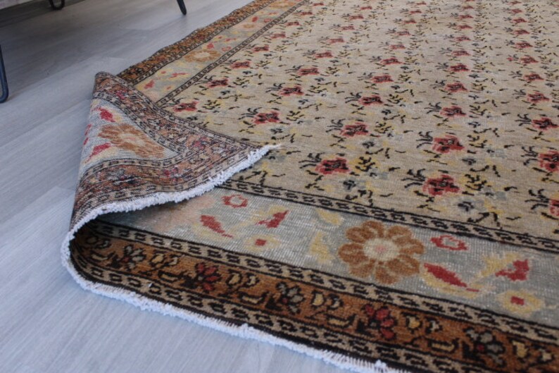 May include: A vintage rug with a floral pattern in shades of beige, brown, and red. The rug has a fringed edge and a detailed border.