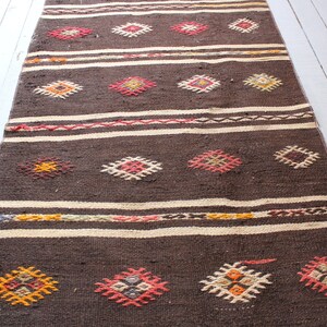 May include: A brown and white woven rug with a geometric pattern. The rug has a traditional design with colorful accents.
