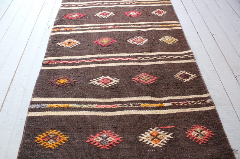 May include: A brown and white woven rug with a geometric pattern. The rug has a traditional design with colorful accents.