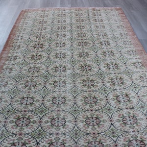May include: A vintage rug with a floral pattern in shades of pink, green, and cream. The rug has a distressed look with faded colors and a worn texture.