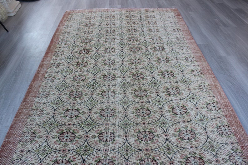 May include: A vintage rug with a floral pattern in shades of pink, green, and cream. The rug has a distressed look with faded colors and a worn texture.