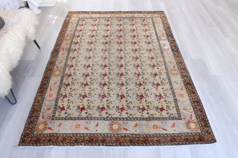 May include: A vintage floral patterned rug with a cream background and a brown, red, and blue border. The rug has a faded look and is in good condition.
