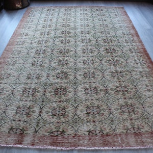 May include: A vintage rug with a cream background and a repeating pattern of pink and green floral motifs. The rug has a red border.