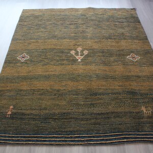 Op de afbeelding: Een groen en bruin vloerkleed met een geometrisch patroon. Het kleed heeft een rand met strepen in blauw, wit en beige.