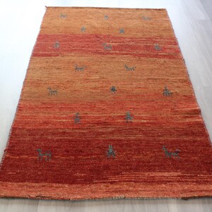 May include: A hand-woven rug with a gradient of orange and red hues. The rug features a repeating pattern of stylized animal figures in a dark blue color.