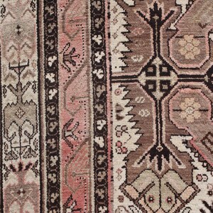 May include: Close-up of a traditional rug with intricate patterns in shades of brown, pink, and white. The rug features a central design with geometric shapes and floral motifs.