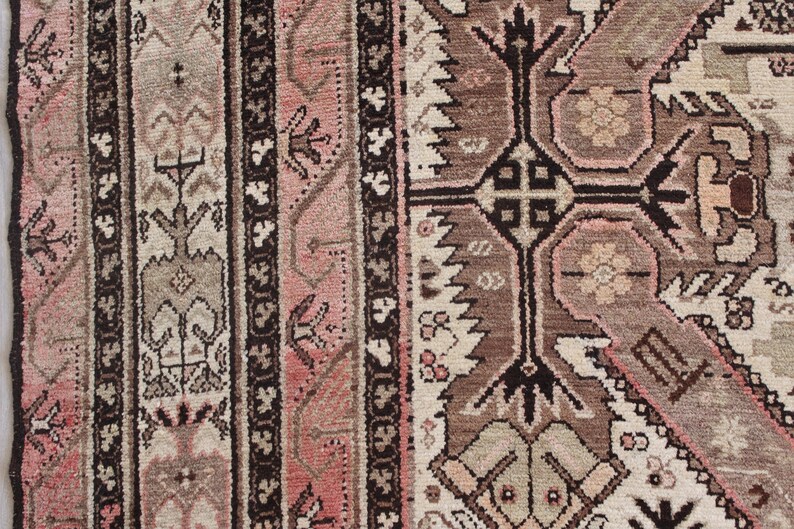 May include: Close-up of a traditional rug with intricate patterns in shades of brown, pink, and white. The rug features a central design with geometric shapes and floral motifs.